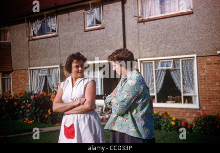 Due madri e i vicini pettegolezzi con le braccia incrociate al di fuori delle loro case su un Essex estate nei primi anni sessanta. Foto Stock
