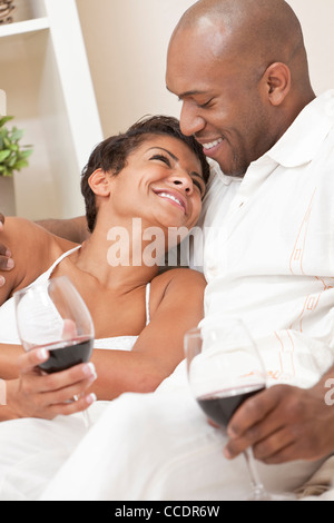 Un felice americano africano l uomo e la donna giovane di trentenni seduti a casa insieme sorridente e bere il vino rosso Foto Stock