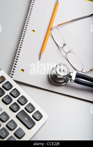 Medico la scrivania con calcolatrice, uno stetoscopio e bicchieri Foto Stock