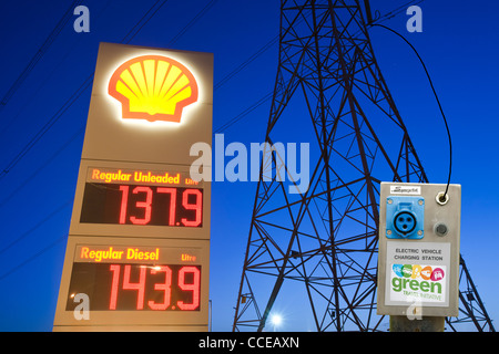 Una benzina sation in Billingham su Teeside, Regno Unito, con un traliccio di elettricità al tramonto e un auto elettrica stazione di ricarica. Foto Stock