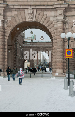 Turisti e residenti di Stoccolma in Svezia a piedi attraverso un arco in pietra vicino al Palazzo Reale nella neve. Foto Stock