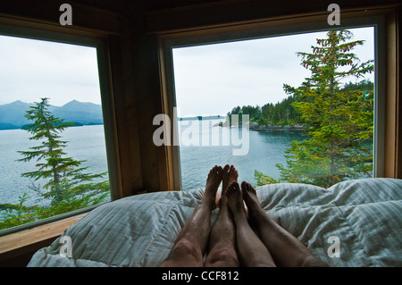 Giovane con i piedi sul letto in camera da letto principale di casa privata su Bamdoroshni Isola, Sitka, Alaska Foto Stock