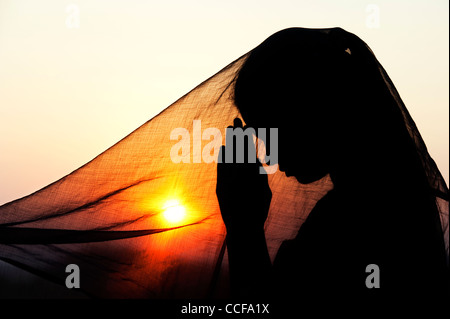 Indian ragazza adolescente pregando al tramonto coperta da un velo. Silhouette. India Foto Stock