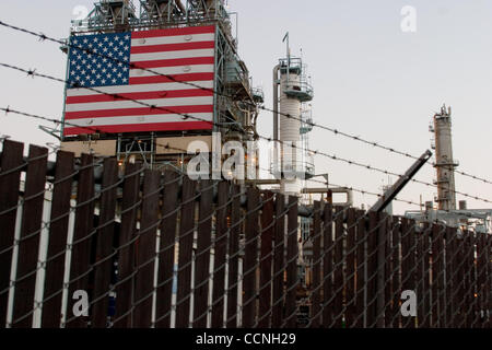 Oct 18, 2004; Long Beach, CA, Stati Uniti d'America; la Conoco philips raffineria di petrolio a Carson nr Long Beach in California con grandi stelle e strisce di bandiera degli Stati Uniti appeso accanto alla enorme chimmney fumaioli. La raffineria ha recinto di sicurezza con filo spinato filo spinato intorno ad esso. La sicurezza è stata aumentata a refinerys attraverso Foto Stock