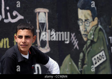 Apr 21, 2010 - Gaza City, nella Striscia di Gaza - palestinesi sedersi davanti a un graffiti raffiguranti catturato soldato israeliano Gilad Shali dipinta da membri di Hamas nel campo profughi di Jabaliya nel nord della striscia di Gaza, 21 aprile 2010. Israele deportati di Ahmad Sabah 40-anno-vecchio prigioniero palestinese per i compressori GA Foto Stock