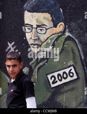 Apr 21, 2010 - Gaza City, nella Striscia di Gaza - palestinesi sedersi davanti a un graffiti raffiguranti catturato soldato israeliano Gilad Shali dipinta da membri di Hamas nel campo profughi di Jabaliya nel nord della striscia di Gaza, 21 aprile 2010. Israele deportati di Ahmad Sabah 40-anno-vecchio prigioniero palestinese per i compressori GA Foto Stock