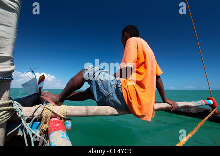 Un pescatore seduto su un tipico malgascio piroga a vela o piroga, vela nel canale del Mozambico, Madagascar. Foto Stock