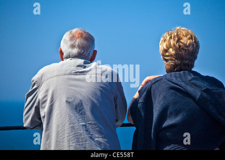 Vista posteriore di mezza età giovane appoggiata sulla ringhiera di un traghetto o una nave da crociera che guarda al mare. Foto Stock