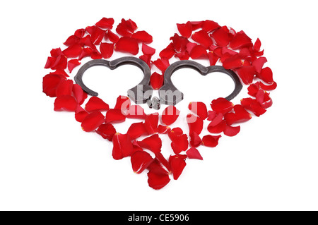 Petali di rosa disposti a forma di cuore e un aperto a forma di cuore in manette Foto Stock