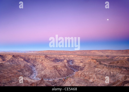 Luna piena impostazione oltre il Fish River Canyon nel sud della Namibia all'alba. Foto Stock