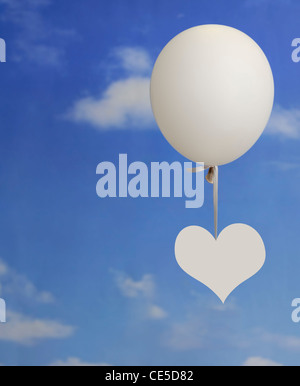 White forma di cuore appeso su un palloncino bianco contro un cielo blu con nuvole Foto Stock