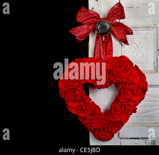 Un Handmade feltro rosso cuore pendente da una porta vintage. Foto Stock