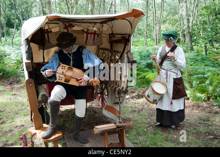 L uomo e la donna vestita come musicisti medievale di fronte ad una tenda con alberi in riproduzione in background organetto di barberia e tamburo Foto Stock