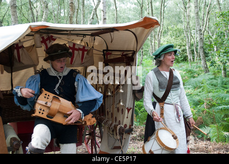 L uomo e la donna vestita come musicisti medievale di fronte ad una tenda con alberi in riproduzione in background organetto di barberia e tamburo Foto Stock