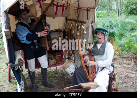 L uomo e la donna vestita come musicisti medievale di fronte ad una tenda con alberi in background la riproduzione di cornamuse e arpa Foto Stock