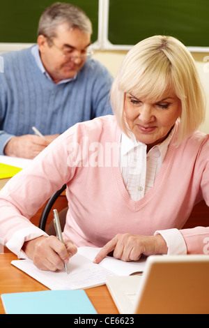 Ritratto di donna bionda rendendo note in copybook senior con uomo sullo sfondo Foto Stock