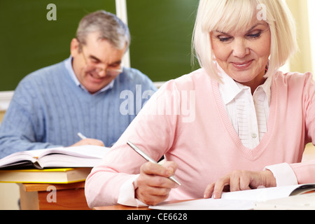 Ritratto di femmina matura rendendo note in copybook senior con uomo sullo sfondo Foto Stock