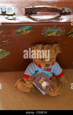 Orsacchiotto di peluche con passaporto sedeva accanto alla vecchia valigia vintage in attesa di andare in vacanza Foto Stock