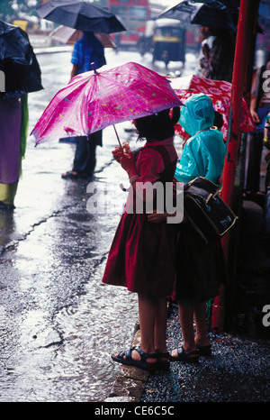 Andando a scuola i bambini ombrelli azienda in piedi alla fermata bus sulla strada in piogge monsoniche ; Mumbai Bombay ; maharashtra ; india Foto Stock