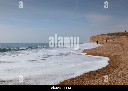 La formazione di schiuma surf sulla spiaggia di Burton Bradstock con i pescatori e con la Jurassic Coast scogliere come sfondo. Foto Stock