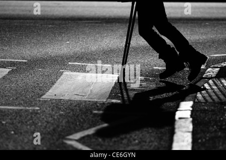 Le gambe di un uomo con le stampelle Come egli attraversa una strada in corrispondenza di un incrocio di zebra Foto Stock