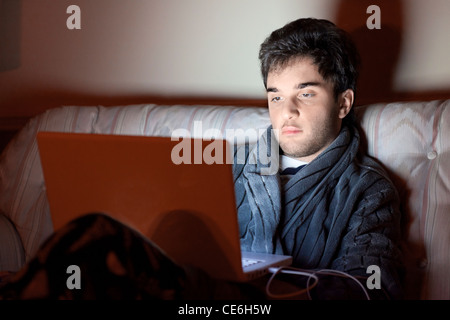 Un giovane uomo si siede su un lettino con un computer portatile sul suo giro. Foto Stock