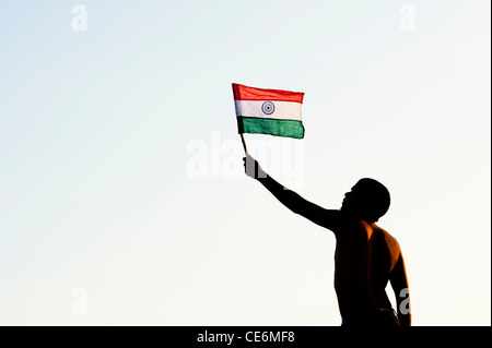 Uomo indiano tenendo una bandiera indiana contro al tramonto in India. Silhouette Foto Stock
