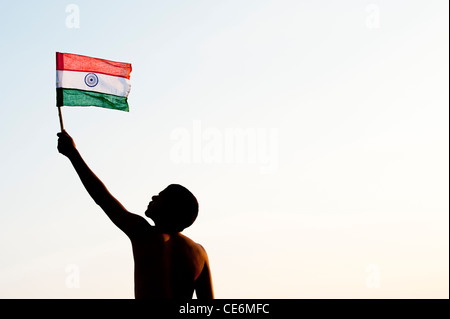 Uomo indiano tenendo una bandiera indiana contro al tramonto in India. Silhouette Foto Stock
