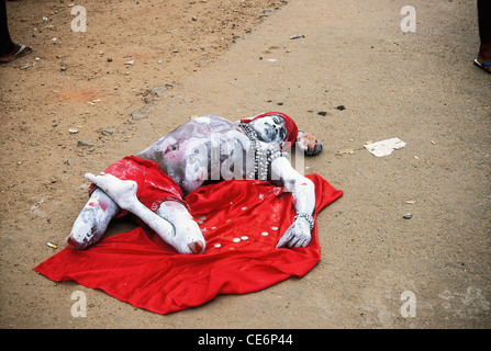 Beggar con amputazione della gamba coperto di cenere rossa panno lombo copricapo rosso giacente sul panno rosso e mendicando ; Kerala ; India Foto Stock