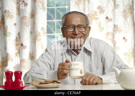 Anziano indiano che tiene una tazza di tè e biscotti in un piatto ; india ; asia ; MR 318 Foto Stock