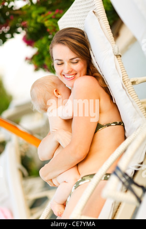 Felice giovane madre posa sul lettino e abbracciando baby Foto Stock
