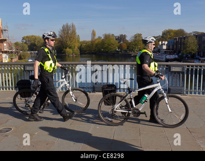 Due poliziotti in giacche fluorescenti wheeling le loro biciclette attraverso Windsor ponte sopra il fiume Tamigi Foto Stock