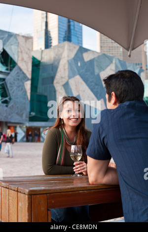Coppia giovane godersi drink presso un bar all'aperto. Federation Square, Melbourne, Victoria, Australia Foto Stock