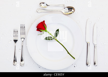 Foto di un luogo tabella di impostazione con una rosa rossa e la scheda vuota sulla piastra. Aggiungi il tuo messaggio al posto di credito. Foto Stock