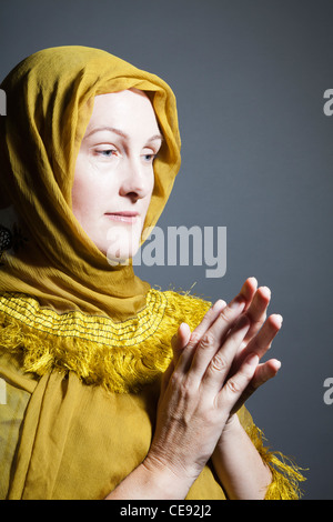 Donna che indossa scialle giallo con le mani nella devozione Foto Stock