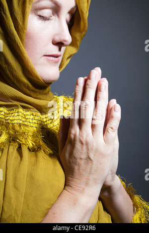 Donna che indossa scialle giallo con le mani nella devozione Foto Stock