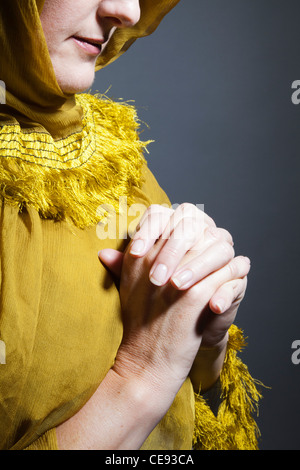 Donna che indossa scialle giallo con le mani nella devozione Foto Stock