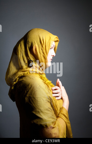 Donna che indossa scialle giallo con le mani nella devozione Foto Stock