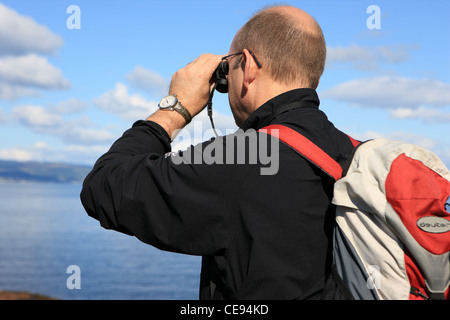 Uomo che guarda al mare attraverso il binocolo Foto Stock