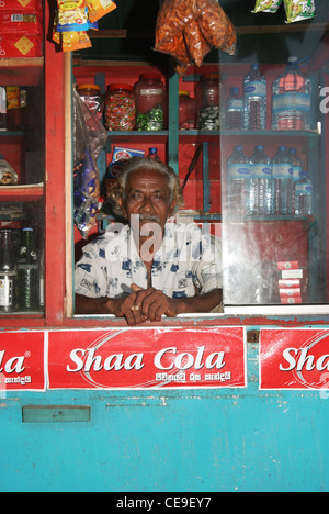 Un dello Sri Lanka uomo che lavora in un punto ristoro che serve bevande e snack, Hiikkaduwa, Sri Lanka. Foto Stock