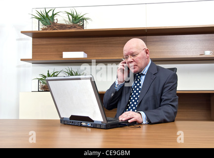 Una società di executive seduto alla sua scrivania, parlando sul suo telefono mobile Foto Stock