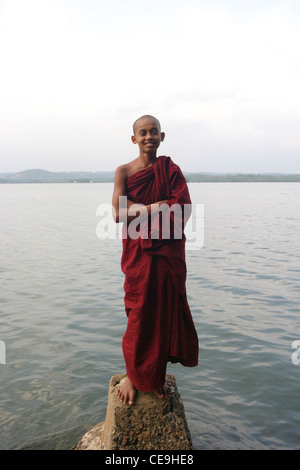 Un giovane monaco buddista sorge proprio di fronte a un lago sorridente Foto Stock