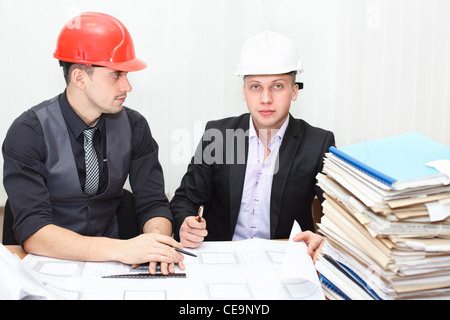 Architetto e ingegnere di costruzione a discutere di piano in ufficio. Popolazione caucasica nei caschi Foto Stock