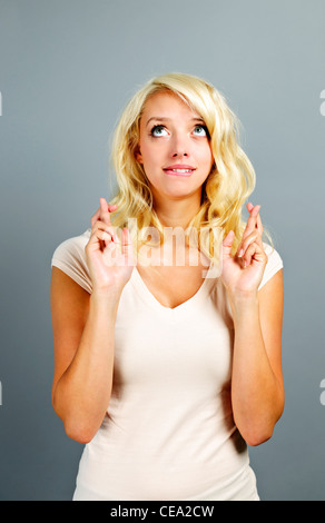 Bionda donna caucasici che desideri con le dita incrociate su sfondo grigio Foto Stock