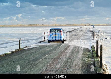 La marea causeway road che conduce al Lindisfarne (santo) Isola con le velme coperta da ghiaccio. Auto a veicolo in marcia. Foto Stock