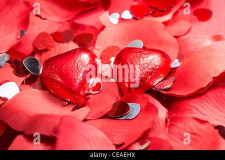 Cuori di cioccolato su falsi petali di colore rosso con decorazioni di cuore Foto Stock