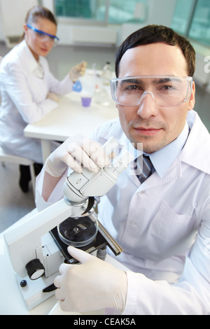 Uomo con un microscopio e il suo collega guardando la fotocamera Foto Stock