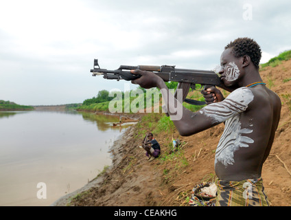 La metà degli adulti dipinte di bianco petto Karo uomo che ha di mira con il fucile Kalashnikov vicino al fiume Torna di Hamer Pastore Etiopia Foto Stock