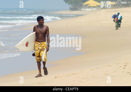 Un locale dello Sri Lanka surfer passeggiate lungo la spiaggia, Hikkaduwa, Sri Lanka Foto Stock