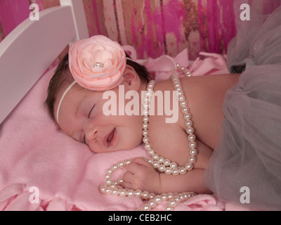 Primo piano di un bellissimo neonato bambina con rosa archetto fiorito, grigio tutu, e perle, lei è sorridente nel suo sonno. Foto Stock